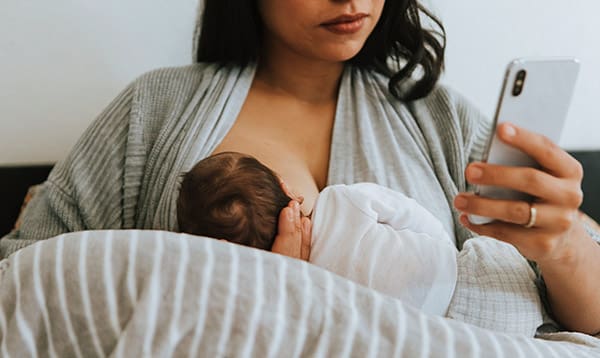 what it really takes to breastfeed a baby- mom with phone while breastfeeding