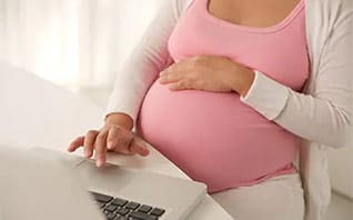 pregnant woman with hand on belly working at laptop