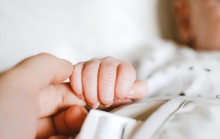 Close-up of a newborn holding an adult's finger, showing newborn reflexes.