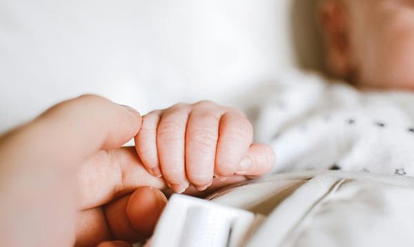 Close-up of a newborn holding an adult's finger, showing newborn reflexes.