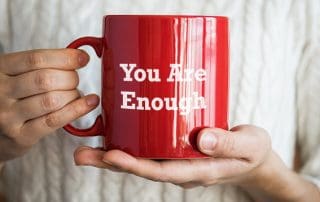 woman holding cup which reads you are enough