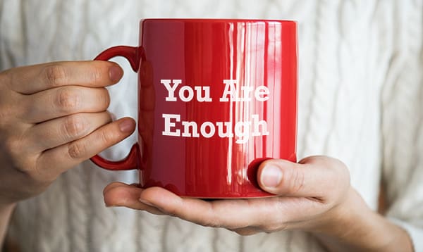 woman holding cup which reads you are enough