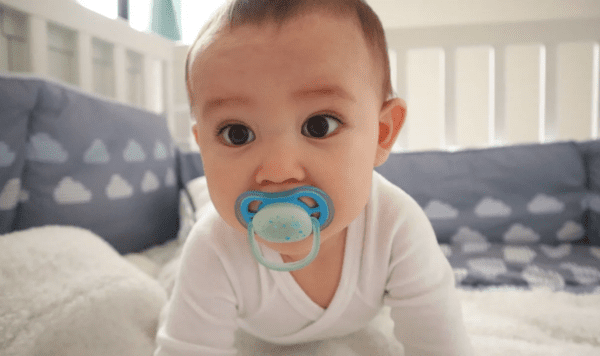 Baby in white onesie with pacifier in mouth.