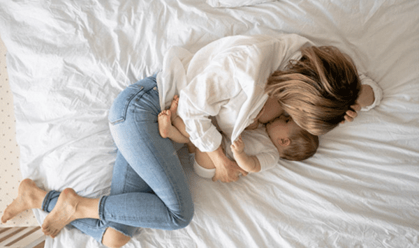 Adult lying on a bed while breastfeeding a baby, highlighting bed sharing and co-sleeping.