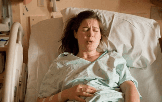 Person lying in a hospital bed, practicing a breathing technique.