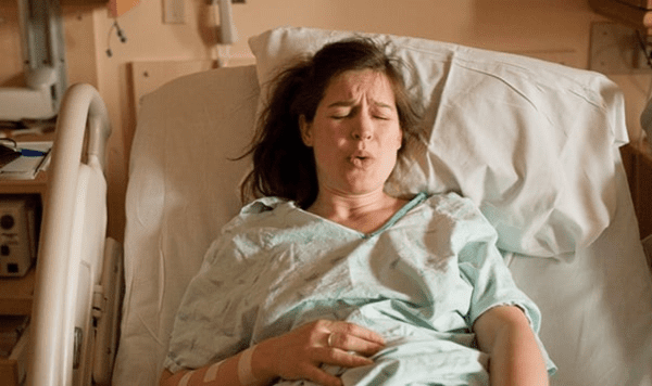 Person lying in a hospital bed, practicing a breathing technique.