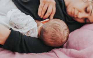 A baby being breastfed during a night feed, lying on a pink blanket.