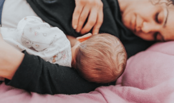 A baby being breastfed during a night feed, lying on a pink blanket.