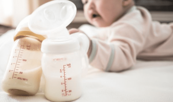 Infant with two baby bottles filled with milk, one with a breast pump attached, used for supplementing breastfeeding.